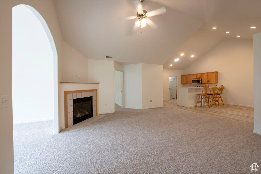 Unfurnished living room featuring light colored carpet, vaulted ceiling, ceiling fan, and a tiled fireplace