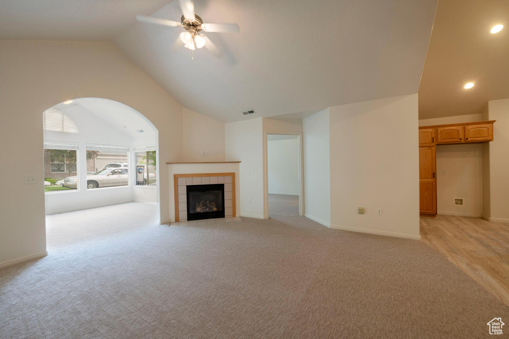 Unfurnished living room with high vaulted ceiling, ceiling fan, a tile fireplace, and light wood-type flooring