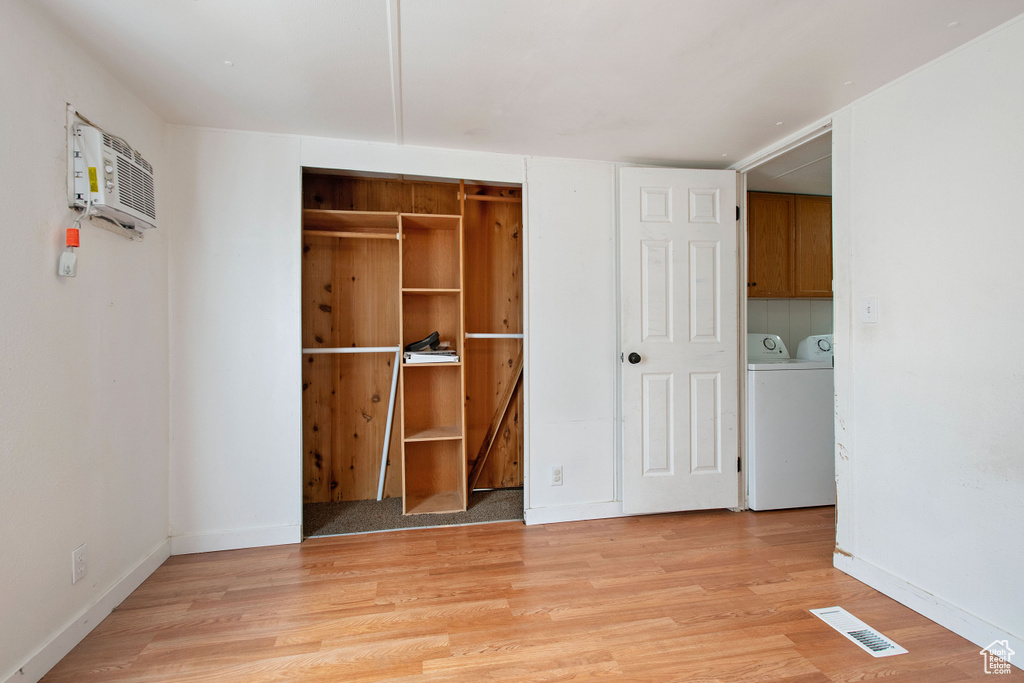 Unfurnished bedroom featuring an AC wall unit, a closet, light hardwood / wood-style floors, and washing machine and clothes dryer