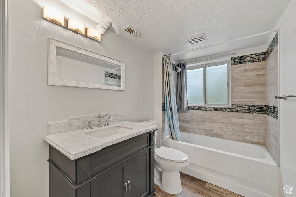 Full bathroom featuring hardwood / wood-style flooring, a textured ceiling, vanity, toilet, and shower / tub combo