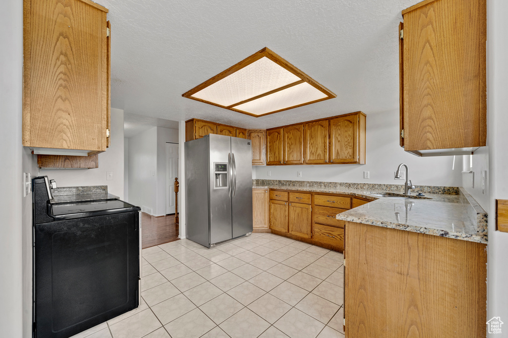 Kitchen featuring sink, black range with electric stovetop, light tile floors, stainless steel refrigerator with ice dispenser, and light stone countertops