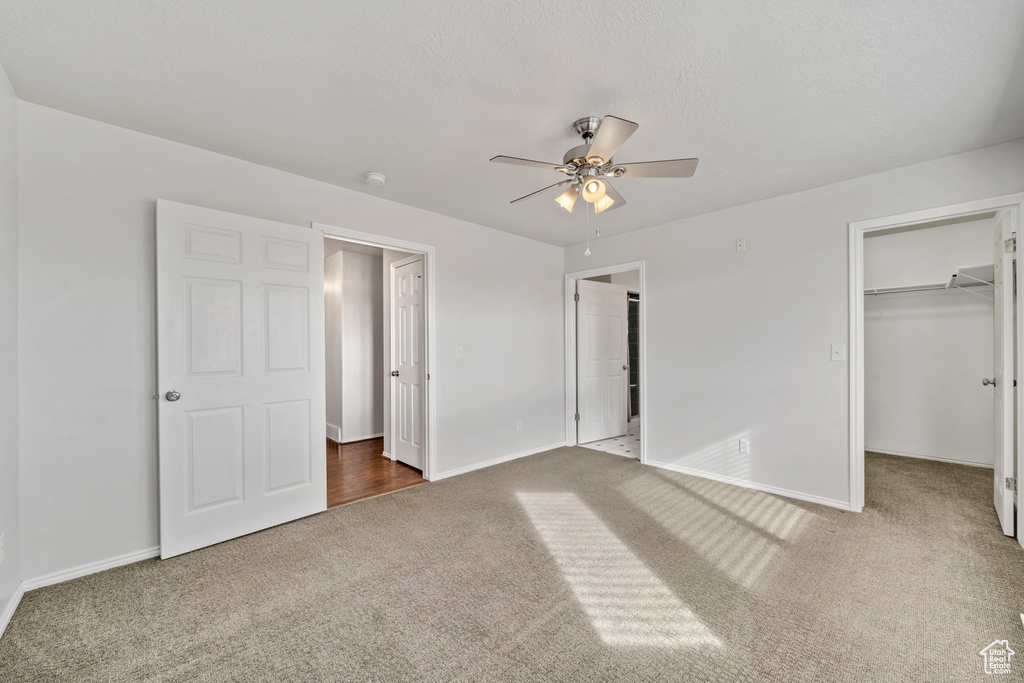 Unfurnished bedroom featuring a spacious closet, a closet, dark carpet, and ceiling fan