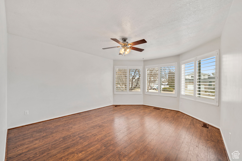 Empty room featuring a textured ceiling, ceiling fan, and dark hardwood / wood-style floors