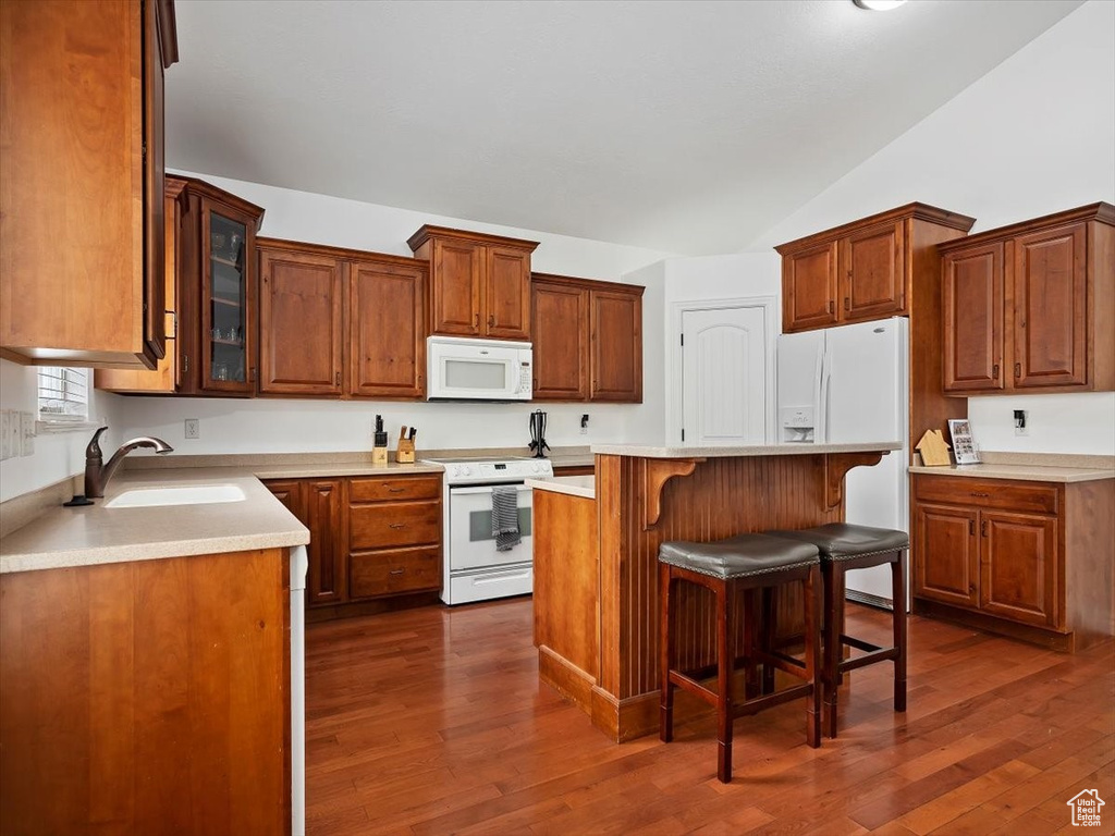 Kitchen with white appliances, vaulted ceiling, dark wood-type flooring, a kitchen breakfast bar, and sink