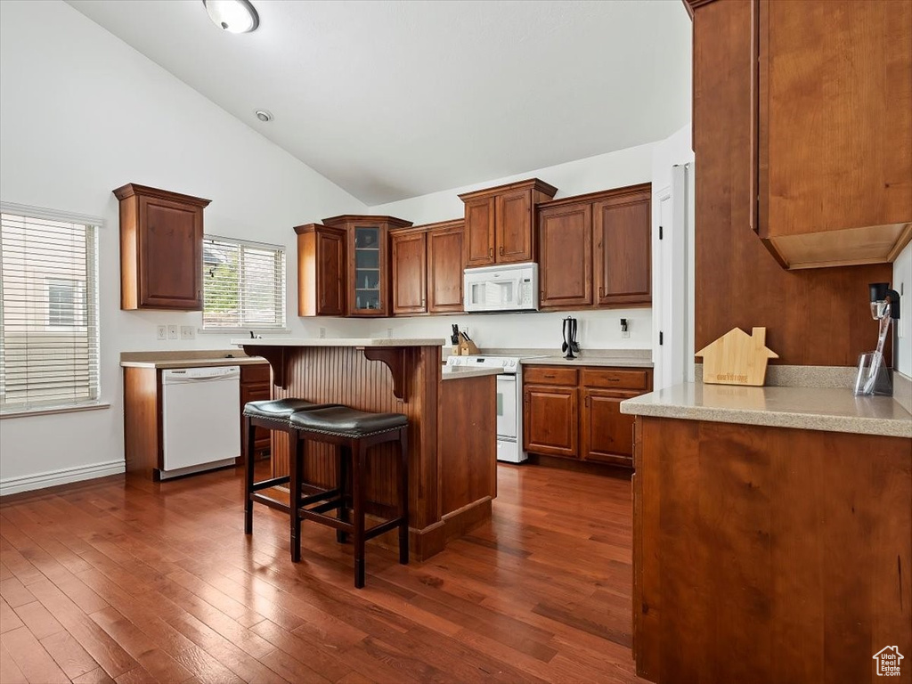 Kitchen with high vaulted ceiling, dark hardwood / wood-style flooring, white appliances, and a breakfast bar