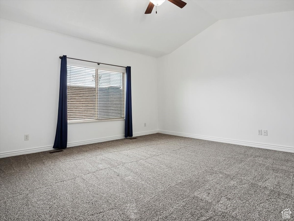 Carpeted empty room featuring ceiling fan and vaulted ceiling