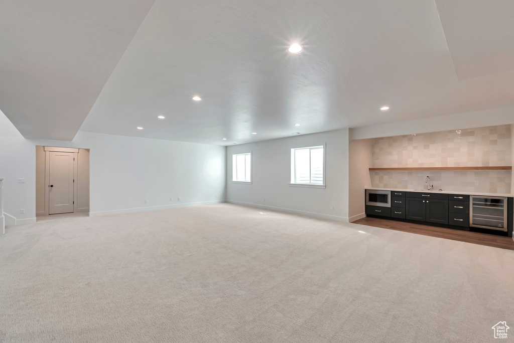 Unfurnished living room featuring light carpet, beverage cooler, and sink