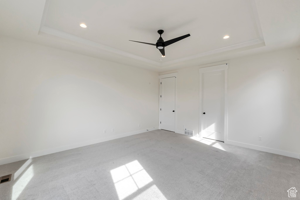 Spare room featuring a raised ceiling, light colored carpet, and ceiling fan