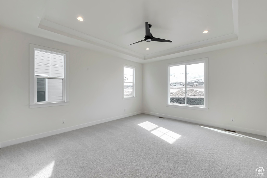 Empty room featuring light colored carpet, a tray ceiling, and ceiling fan