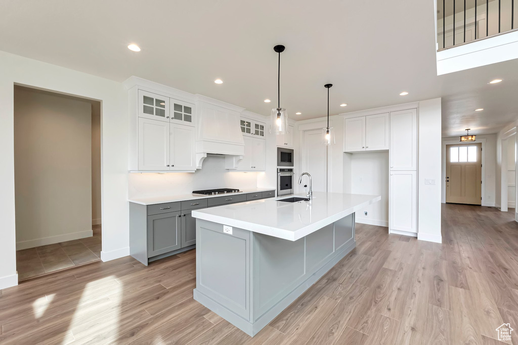 Kitchen with light wood-type flooring, pendant lighting, a kitchen island with sink, and gray cabinetry