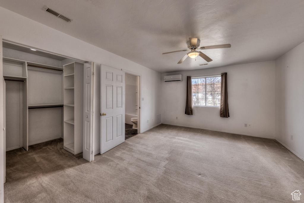 Unfurnished bedroom with connected bathroom, ceiling fan, a closet, a wall mounted AC, and dark colored carpet