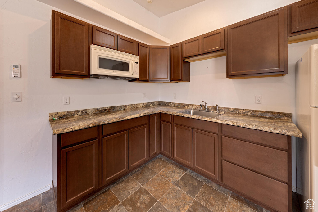 Kitchen featuring dark tile flooring, white appliances, sink, and dark brown cabinets