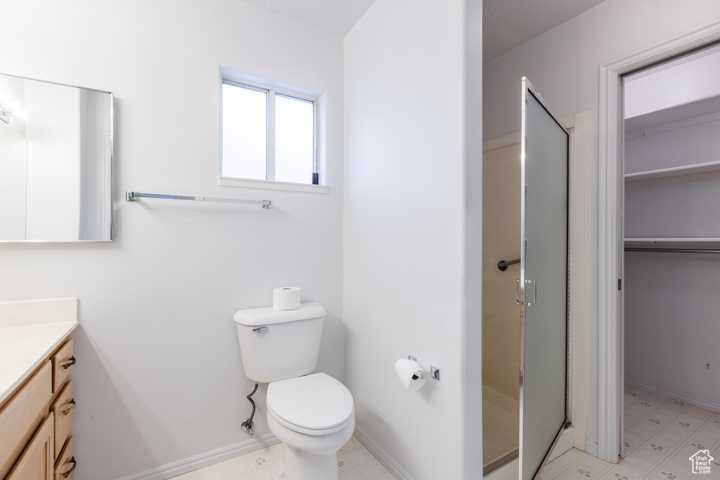 Bathroom featuring tile flooring, a shower with door, toilet, and vanity