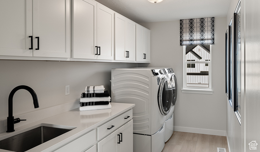 Washroom featuring independent washer and dryer, sink, cabinets, and light hardwood / wood-style floors