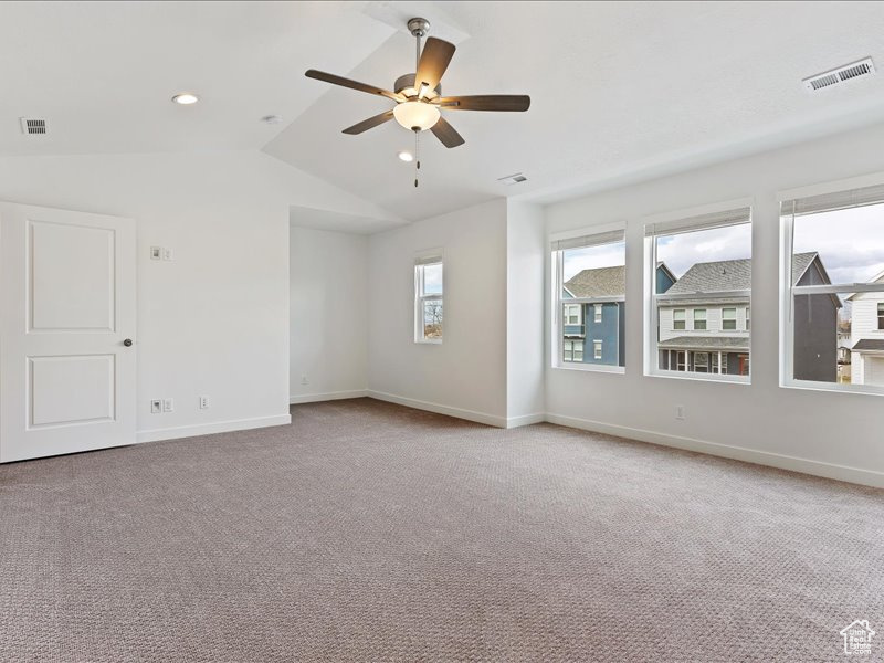 Empty room with vaulted ceiling, light colored carpet, and ceiling fan