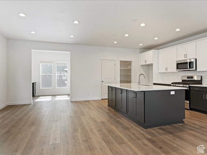 Kitchen with appliances with stainless steel finishes, a center island with sink, white cabinetry, and light hardwood / wood-style floors