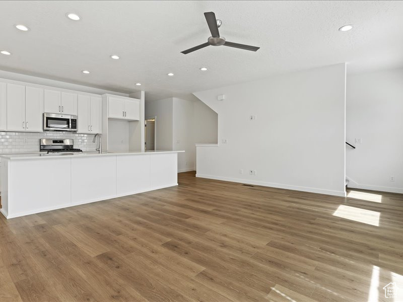 Kitchen featuring ceiling fan, range, light hardwood / wood-style flooring, backsplash, and white cabinets