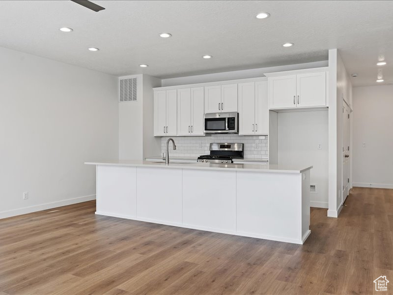 Kitchen with white cabinets, appliances with stainless steel finishes, an island with sink, and hardwood / wood-style flooring