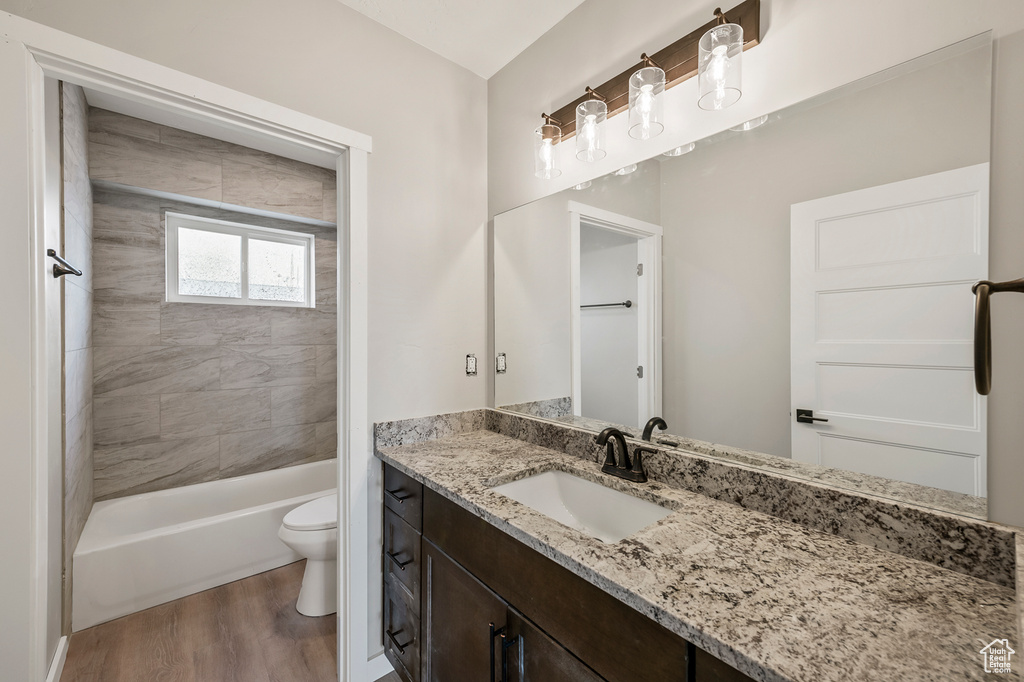 Full bathroom featuring tiled shower / bath, oversized vanity, hardwood / wood-style floors, and toilet
