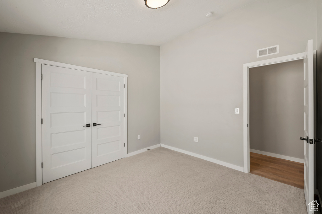 Unfurnished bedroom featuring vaulted ceiling, a closet, and light colored carpet