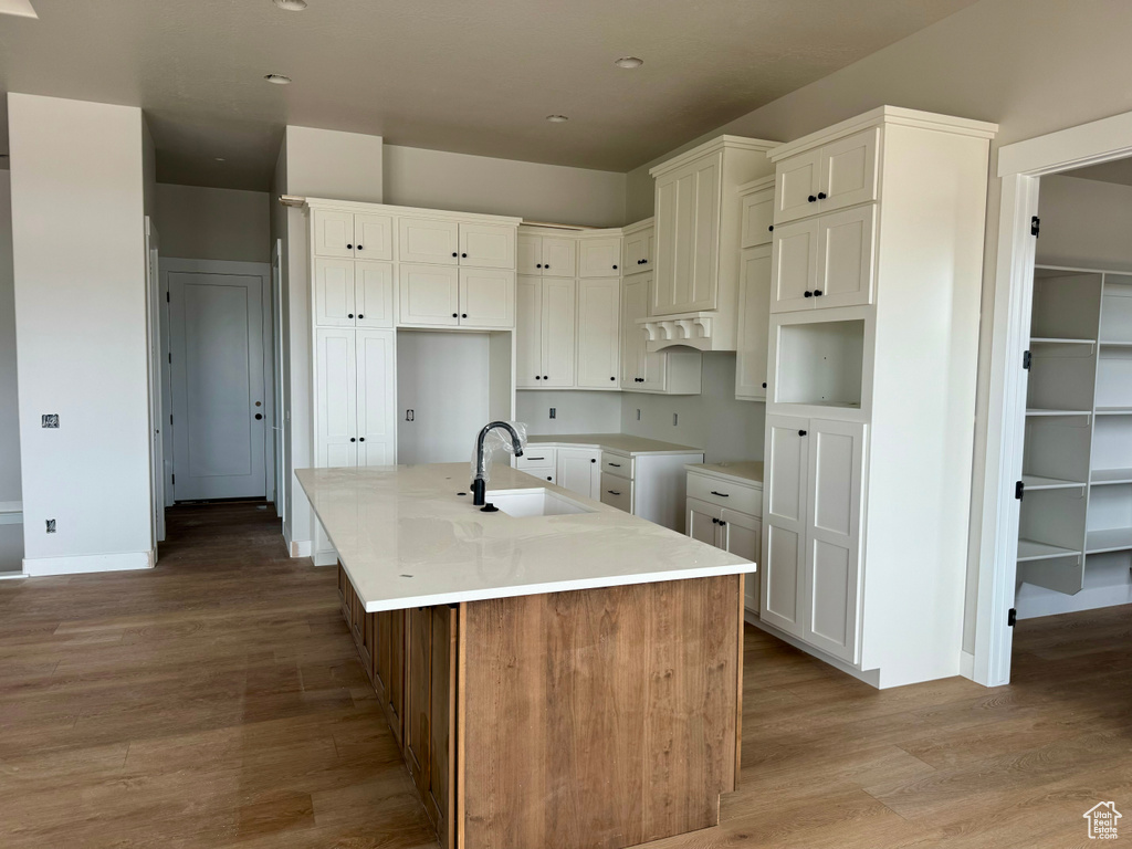 Kitchen with white cabinets, a kitchen island with sink, hardwood / wood-style flooring, and sink