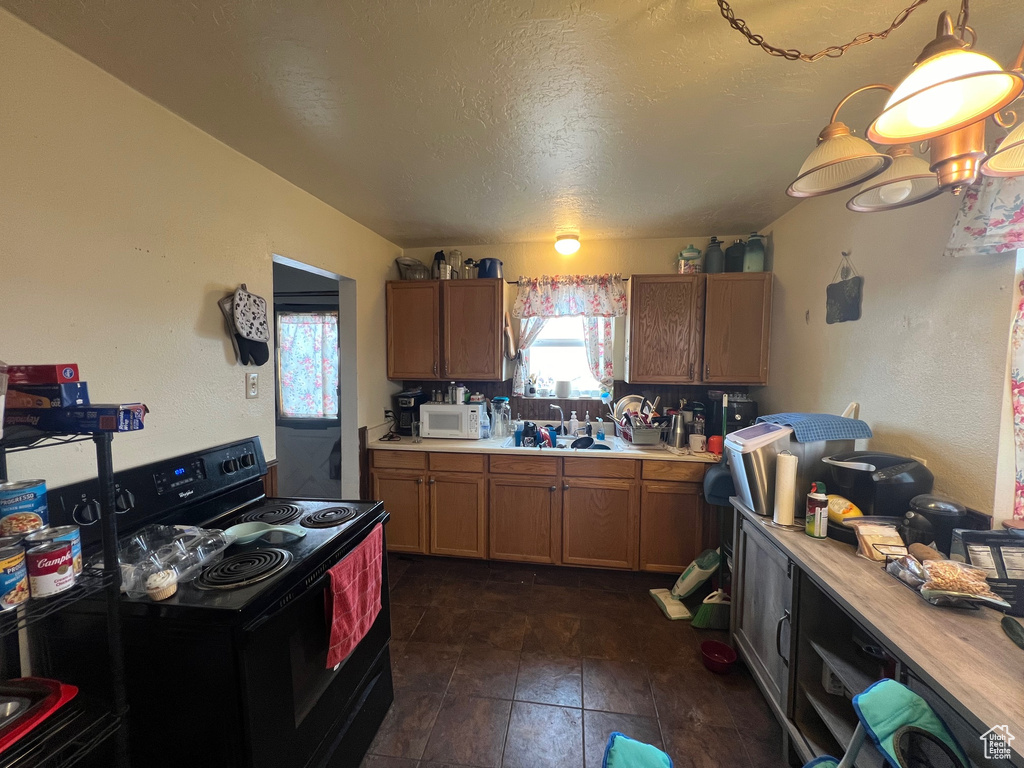 Kitchen featuring dark tile flooring, sink, pendant lighting, and black electric range oven