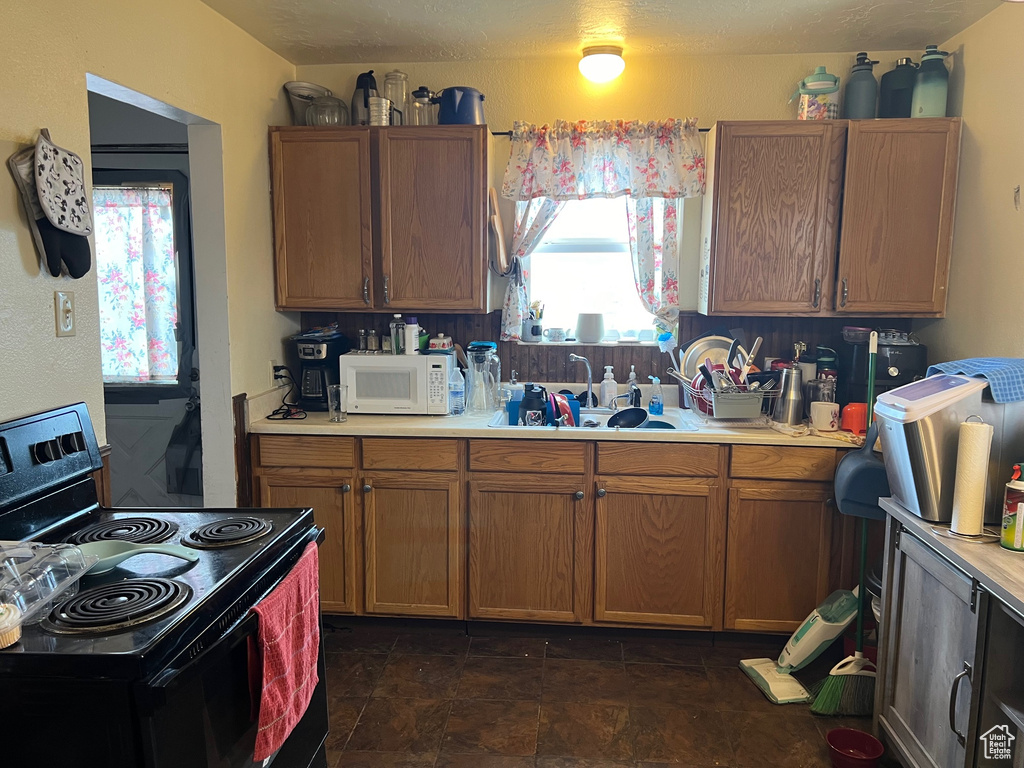 Kitchen with sink, plenty of natural light, black electric range oven, and dark tile floors