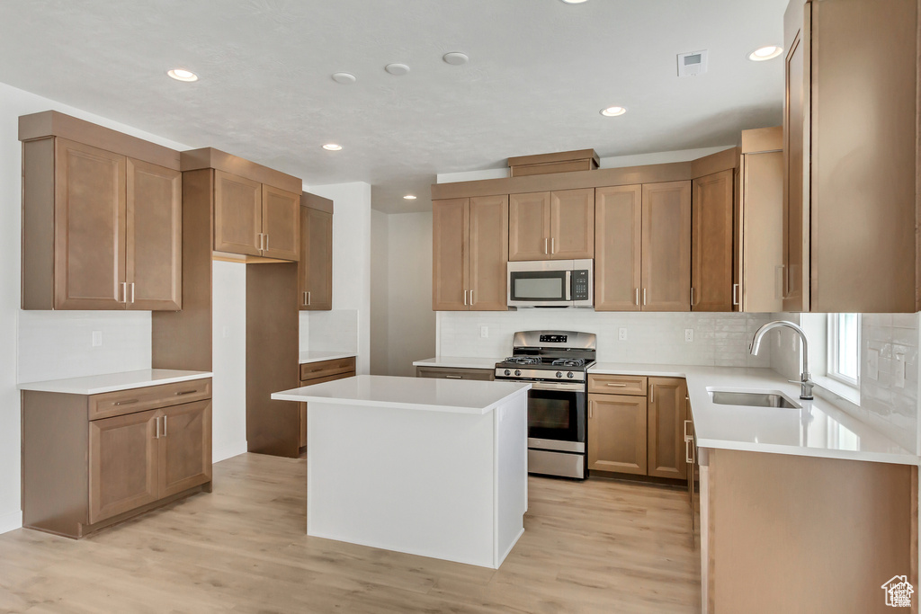 Kitchen with a center island, sink, backsplash, appliances with stainless steel finishes, and light wood-type flooring