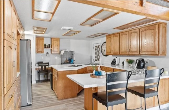 Kitchen with a kitchen island, stainless steel refrigerator, electric stovetop, a kitchen bar, and light hardwood / wood-style flooring