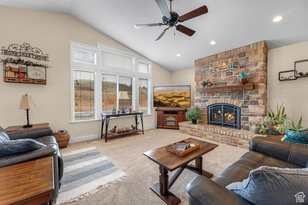 Living room featuring a fireplace, light carpet, vaulted ceiling, and ceiling fan