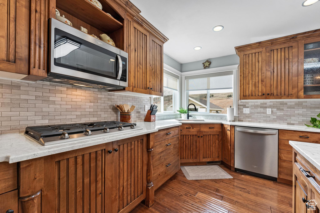 Kitchen with backsplash, stainless steel appliances, light stone countertops, and dark hardwood / wood-style floors