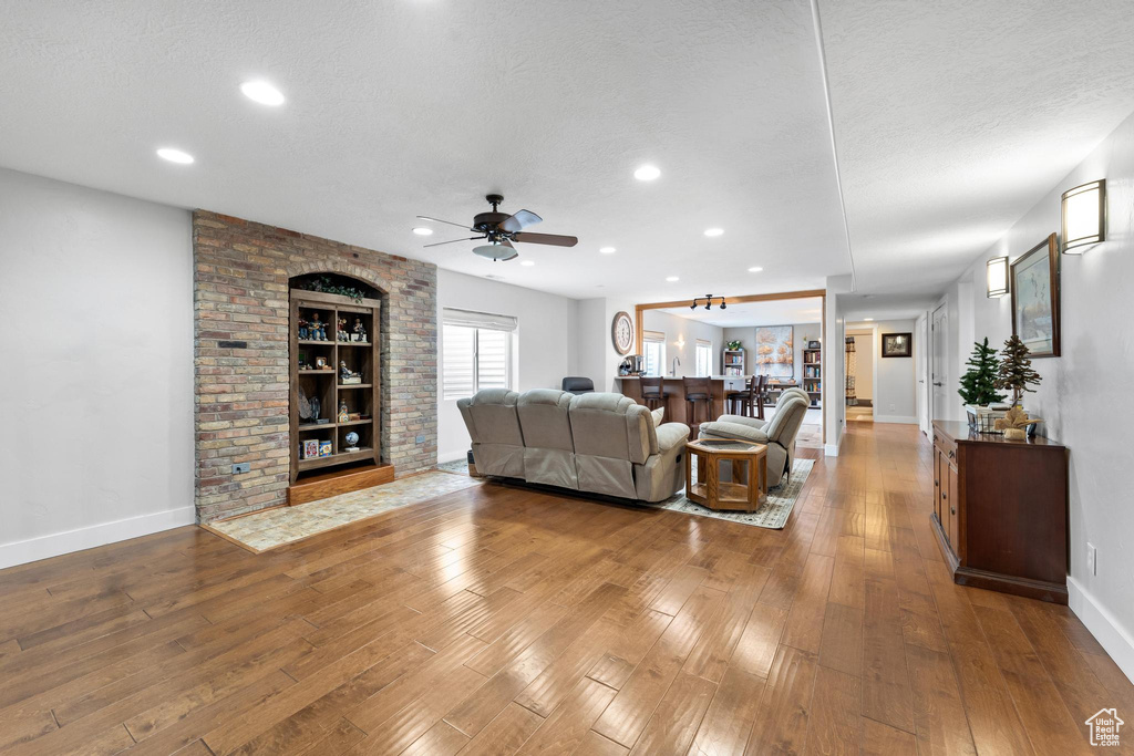 Living room with built in features, ceiling fan, a textured ceiling, and hardwood / wood-style floors