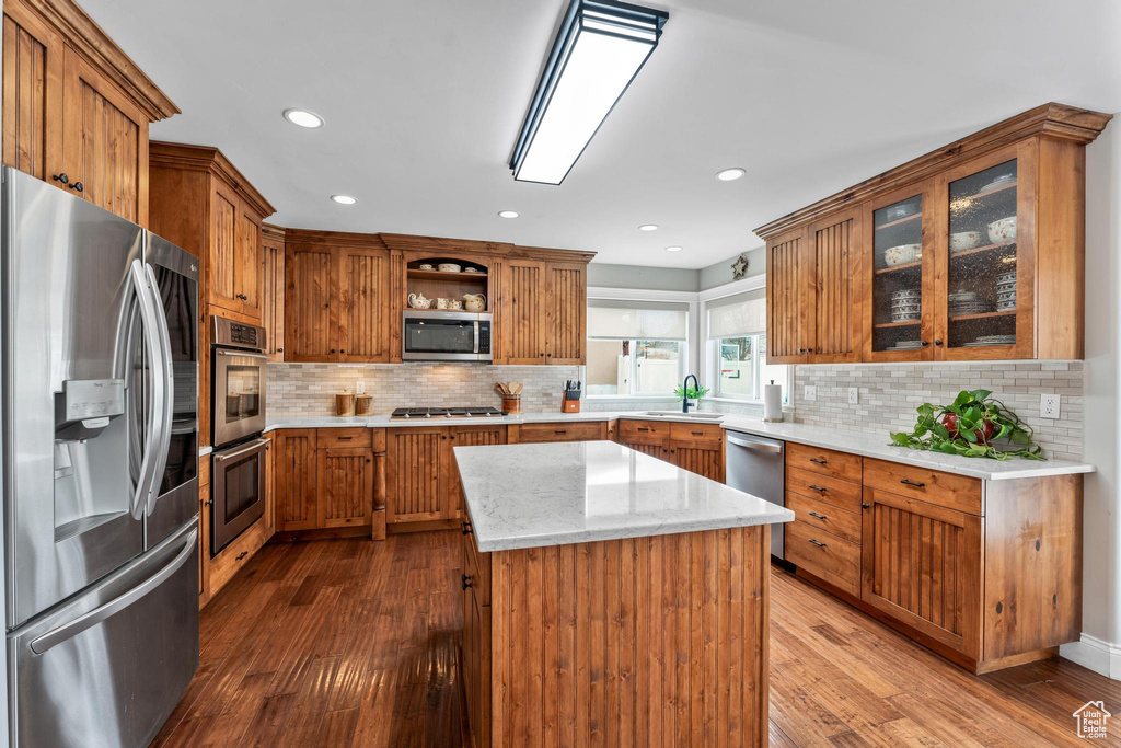 Kitchen featuring tasteful backsplash, hardwood / wood-style floors, sink, light stone countertops, and stainless steel appliances