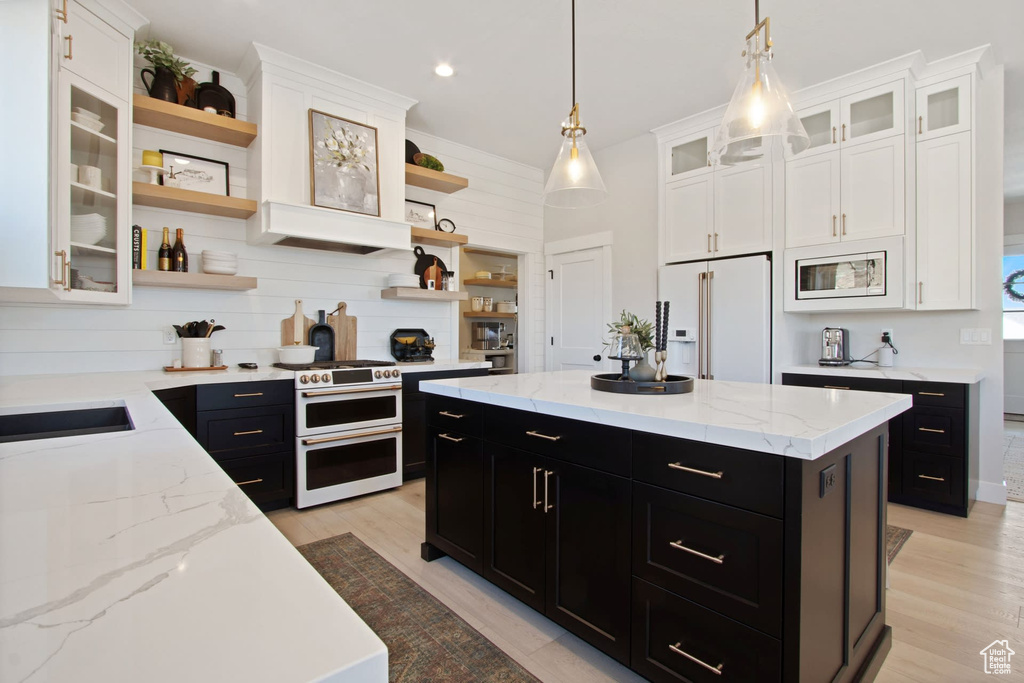 Kitchen with a center island, white appliances, pendant lighting, light wood-type flooring, and light stone counters
