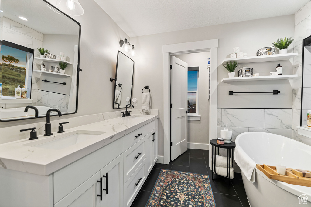 Bathroom with tile walls, a bath, double sink vanity, and tile floors