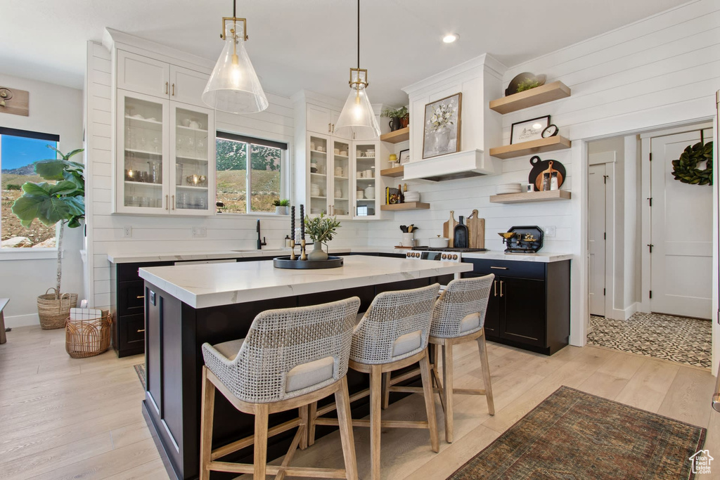 Kitchen featuring white cabinetry, a center island, hanging light fixtures, a kitchen bar, and light hardwood / wood-style flooring