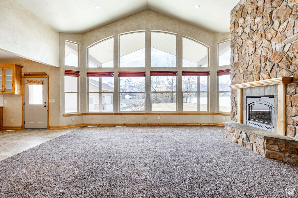 Unfurnished living room featuring a stone fireplace, light colored carpet, plenty of natural light, and high vaulted ceiling