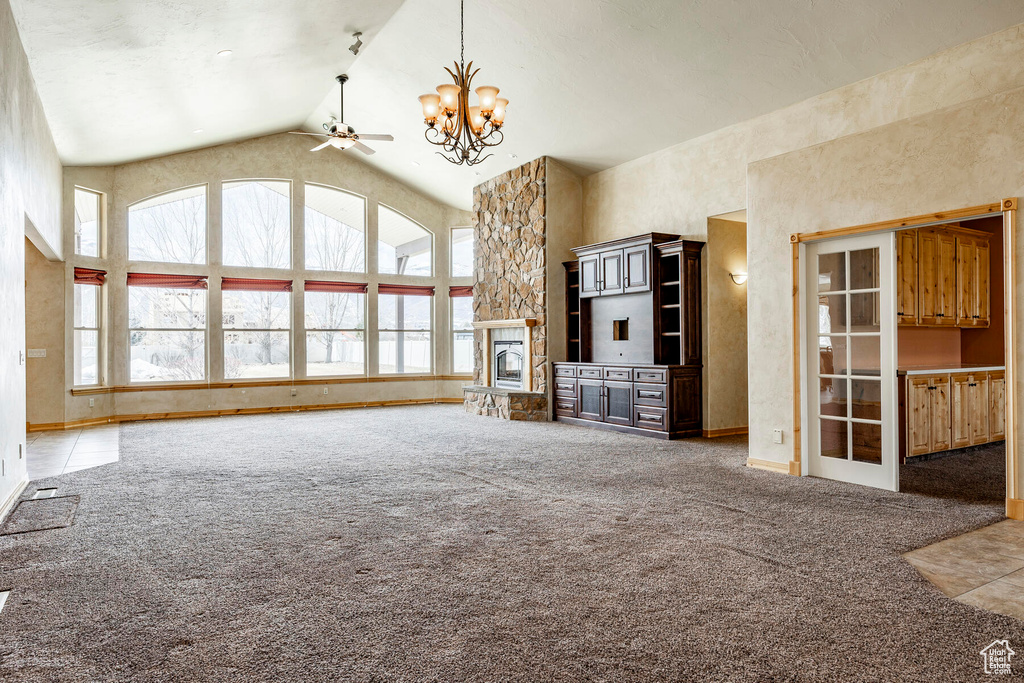 Unfurnished living room featuring light tile floors, high vaulted ceiling, ceiling fan with notable chandelier, and a fireplace