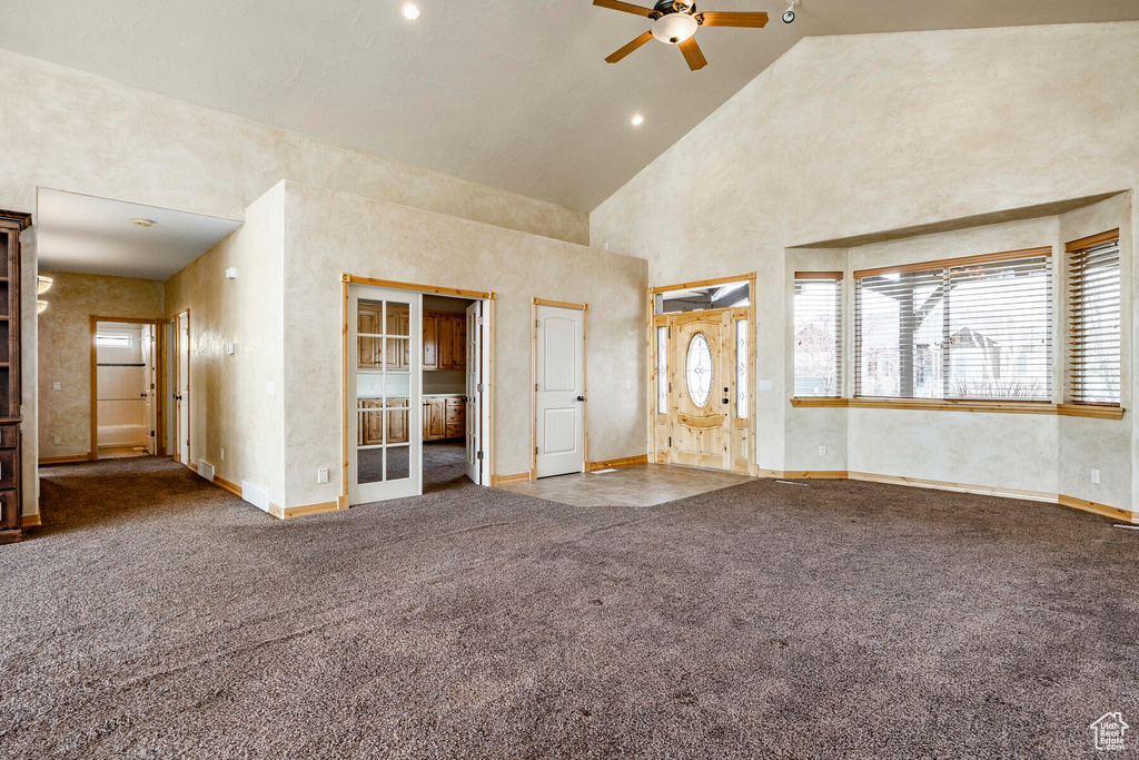 Unfurnished living room featuring high vaulted ceiling, dark colored carpet, and ceiling fan