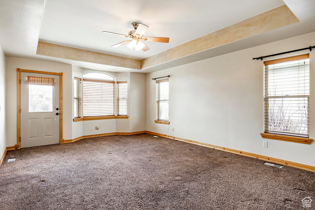 Empty room with a raised ceiling, carpet floors, and ceiling fan
