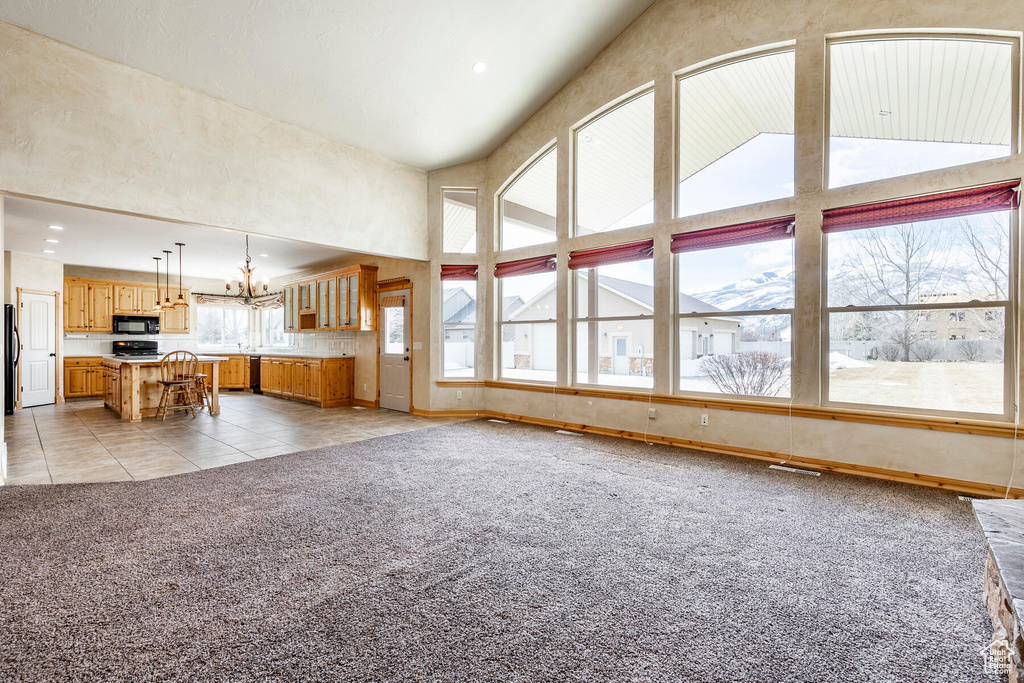 Unfurnished living room featuring high vaulted ceiling, light carpet, and a notable chandelier