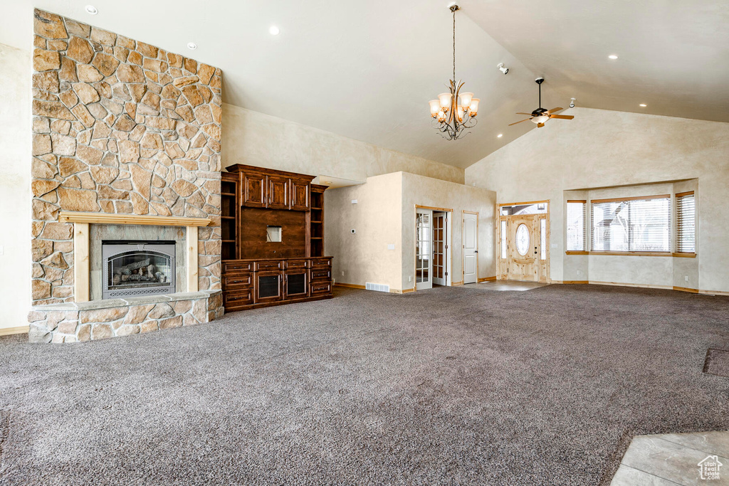Unfurnished living room featuring high vaulted ceiling, light carpet, a stone fireplace, and ceiling fan with notable chandelier