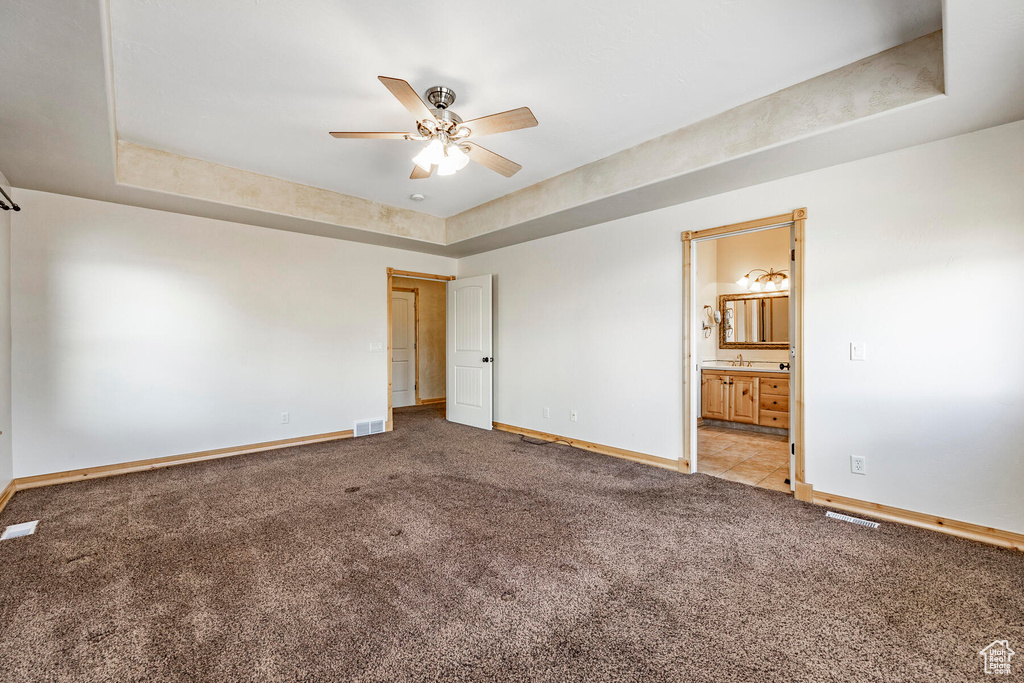 Unfurnished bedroom featuring light carpet, ceiling fan, and a raised ceiling