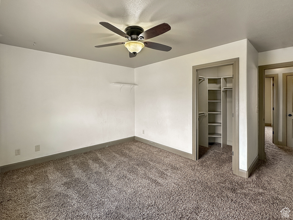 Unfurnished bedroom with a walk in closet, ceiling fan, a closet, and dark carpet