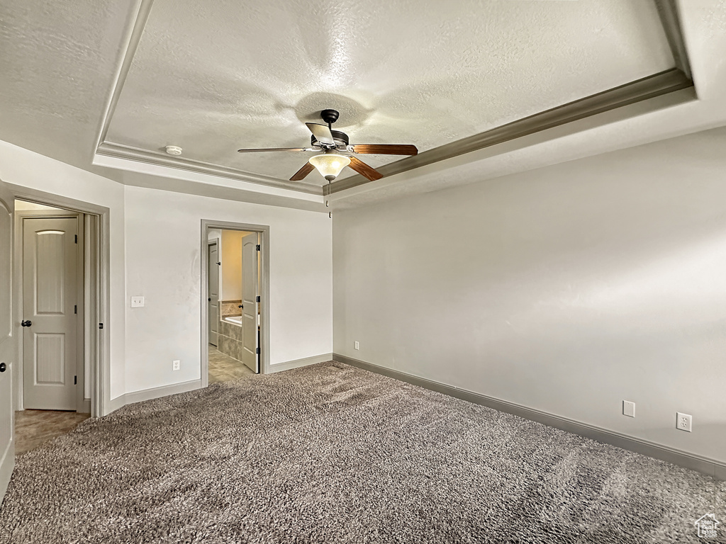 Unfurnished room featuring a textured ceiling, a tray ceiling, light colored carpet, and ceiling fan