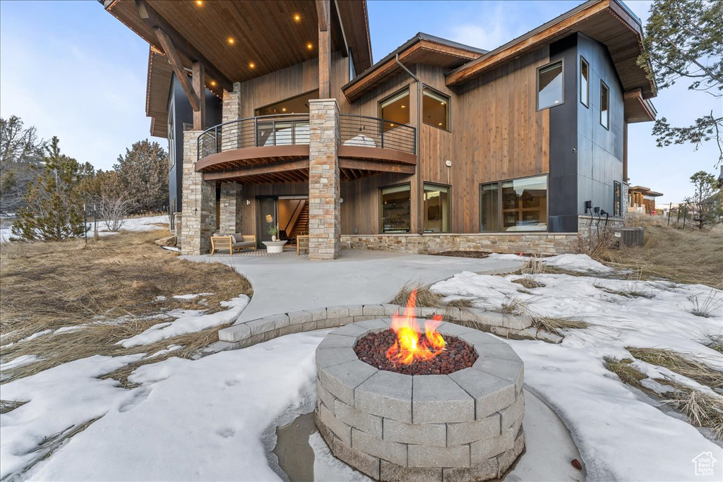 Snow covered house featuring central AC unit, an outdoor fire pit, and a balcony