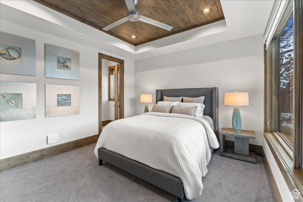 Bedroom with dark colored carpet, a raised ceiling, ceiling fan, and wooden ceiling