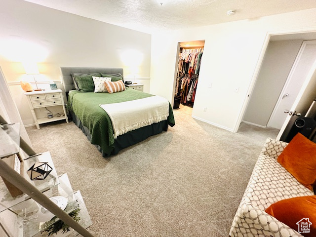 Bedroom featuring a textured ceiling, light carpet, a closet, and a walk in closet