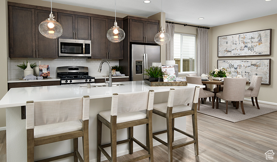 Kitchen with backsplash, stainless steel appliances, a kitchen breakfast bar, and hanging light fixtures