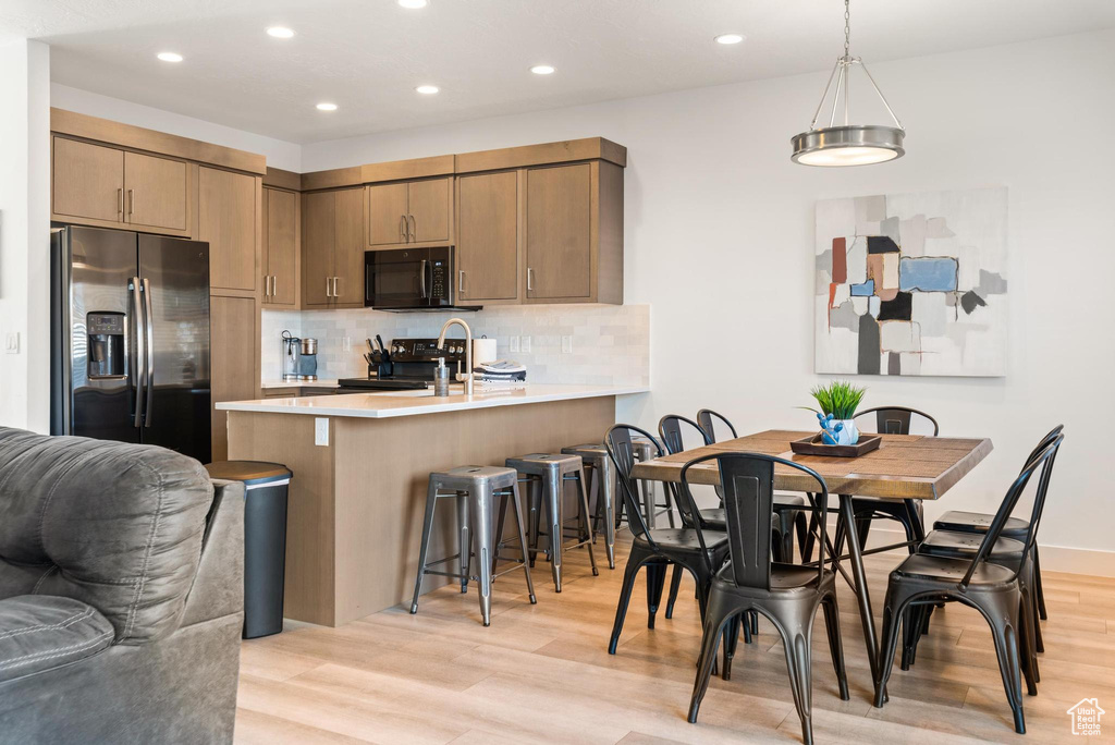 Kitchen featuring tasteful backsplash, light hardwood / wood-style floors, stove, hanging light fixtures, and stainless steel refrigerator with ice dispenser